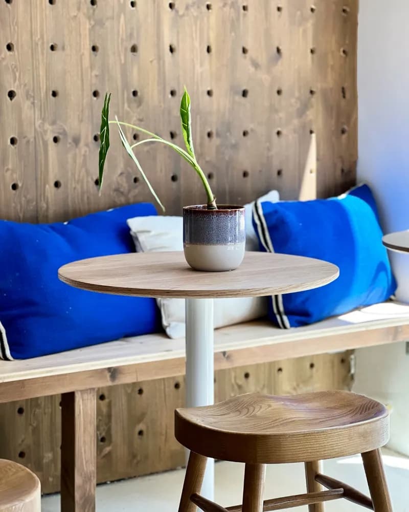 Banquette en bois clair avec coussins bleu Klein devant un panneau de bois perforé, plante sur la table