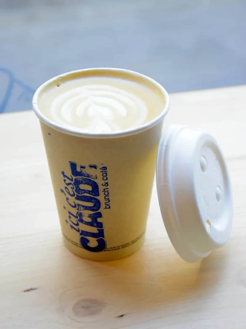 Gobelet kraft « ici c'est Claude » rempli d'un latte au beau latte art, posé sur une table en bois