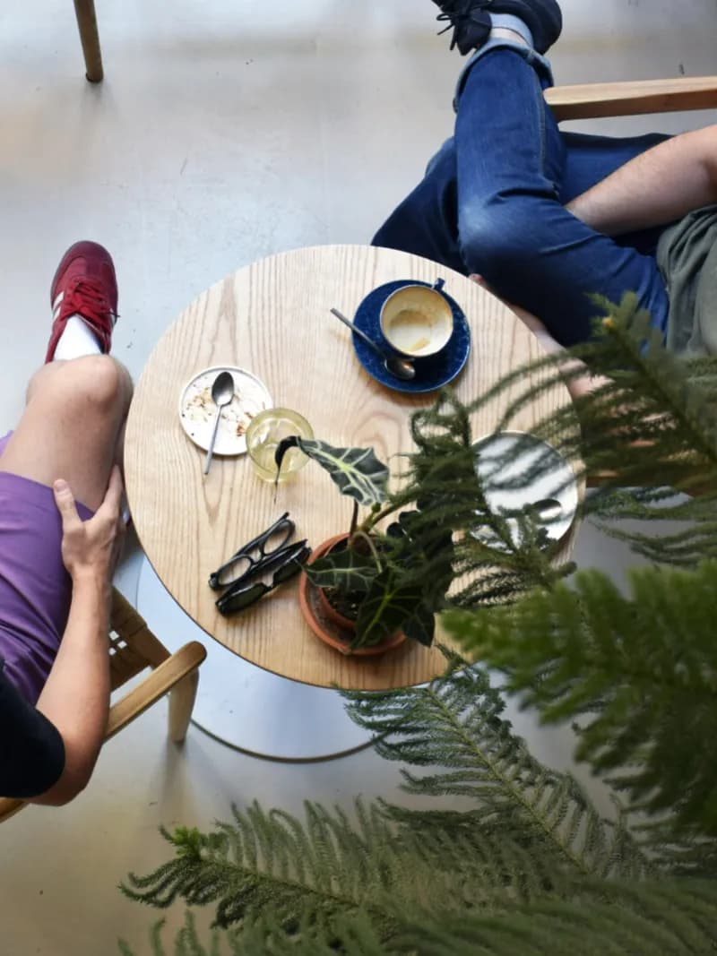 Vue plongeante sur les tables du comptoir vitrine : cafés, plantes et clientes en pleine discussion